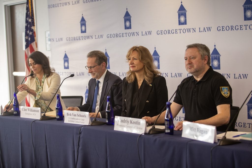 Four panelists sit at a long table at an event discussing war crimes in Ukraine.