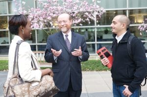 Dean Treanor speaks to two students with cherry blossoms in the background outside of Hotung.