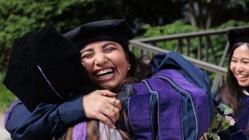Two women in graduation regalia, embracing