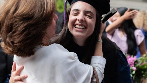 A woman embraces a younger woman in graduation regalia