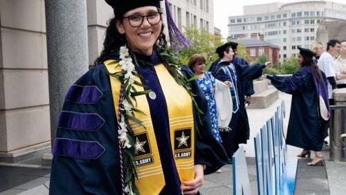 A woman in graduation regalia wearing a yellow stole with the U.S. Army logo on it