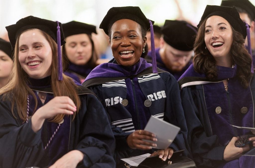 A row of smiling students in graduation regalia