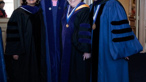 Four people standing together, wearing academic robes