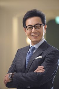 A man with dark hair, wearing eyeglasses and a gray suit