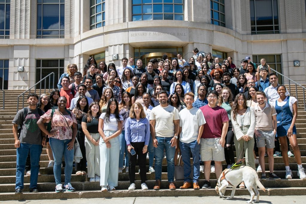 A group of students and one service dog posing for a group photo outside McDonough Hall