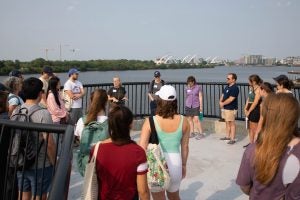 Students and a professor stand in a circle on an overlook by the Anacostia River