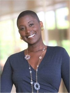 Image of a smiling Black woman with short hair, wearing a blue shirt and long necklace
