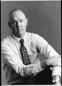 A black and white photo of a man with short hair, wearing a shirt and tie