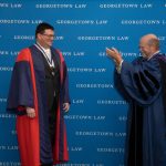 Two men standing, in academic regalia, one applauding the other