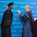 A man preparing to put a medal around the neck of a woman. Both are wearing academic regalia.