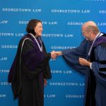 A woman and man wearing academic regalia and shaking hands