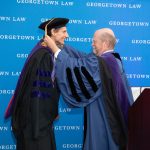 Two men in academic regalia, one placing a medal around the neck of the other.