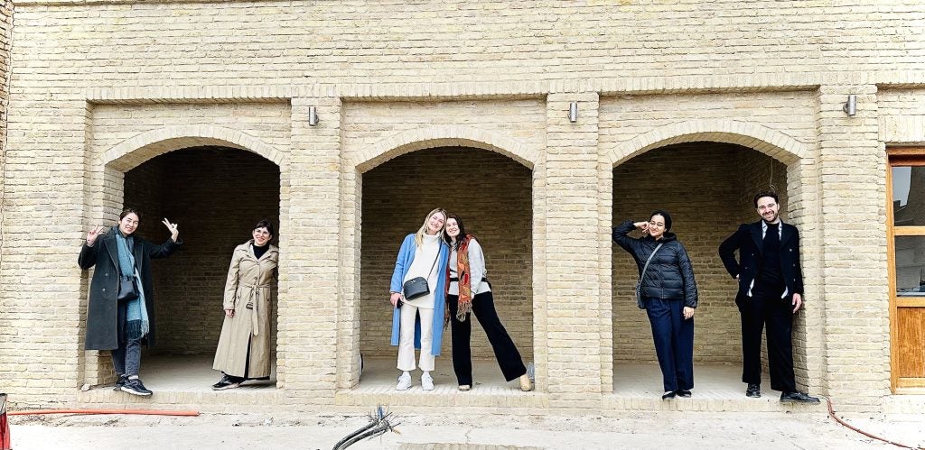 Six students standing in the archways of a brick building