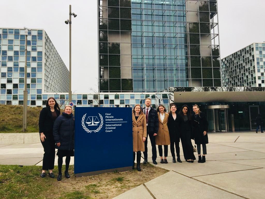 A row of people standing by a sign outside a building