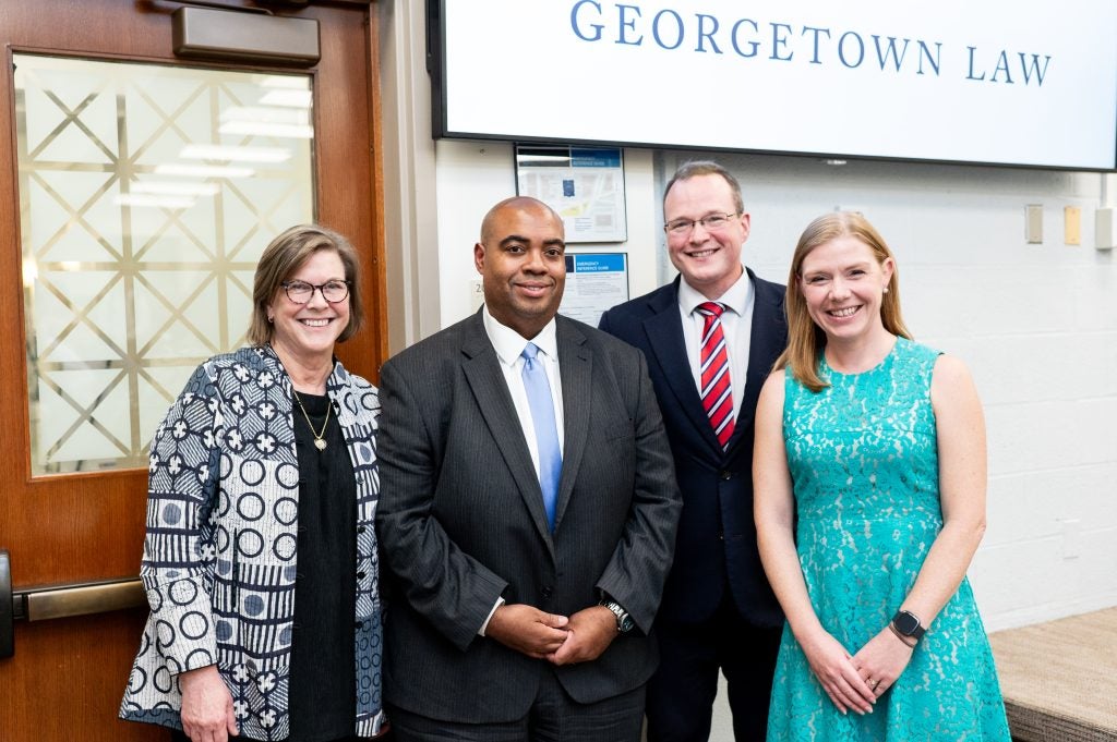 Two men and two women pose together in a Georgetown Law classroom.