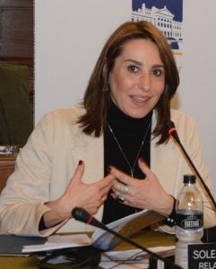 A woman wearing a dark turtleneck and light blazer