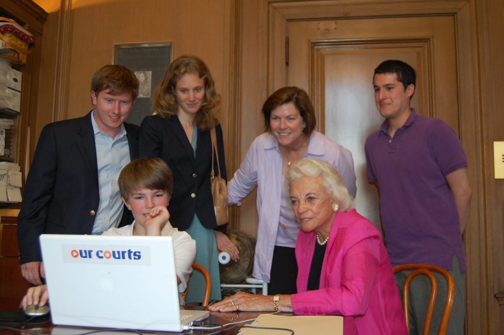 A young boy showing Justice Sandra Day O'Connor a video game on a computer, with several other people watching from behind. 