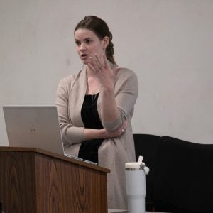 A woman with long dark hair speaking to students in a classroom