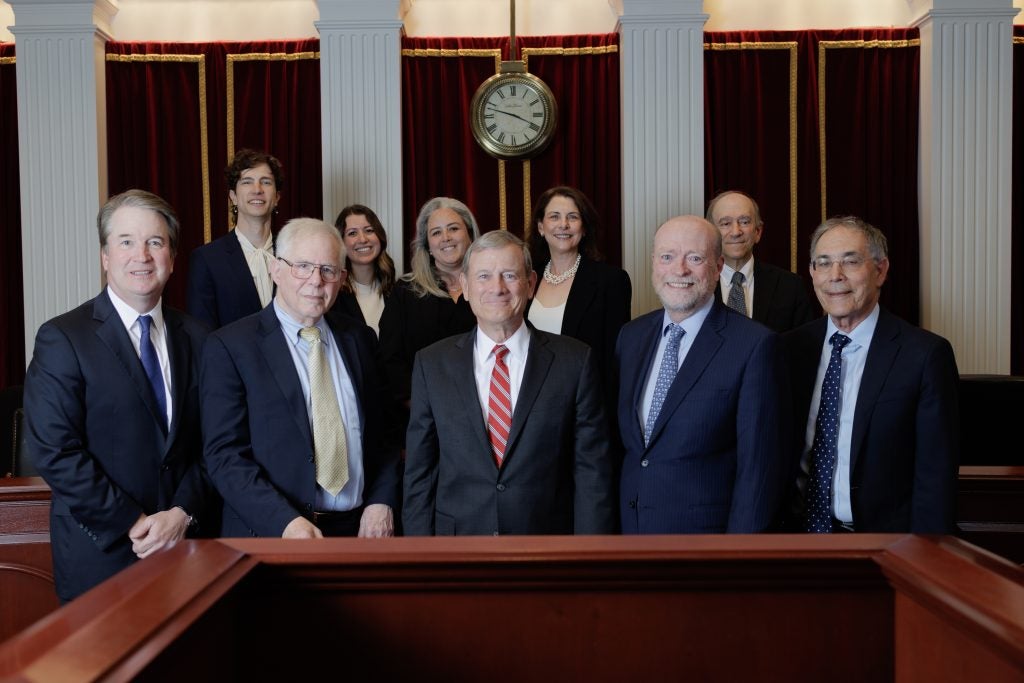 A group of people standing in two rows, in a formal moot courtroom setting. Supreme Court Justice Brett Kavanaugh and Chief Justice John Roberts are both in the front row.