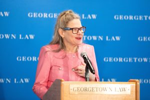 A woman in a pink jacket speaking at a podium