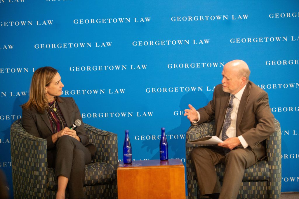 A man and woman sitting in armchairs on a stage and speaking to each other