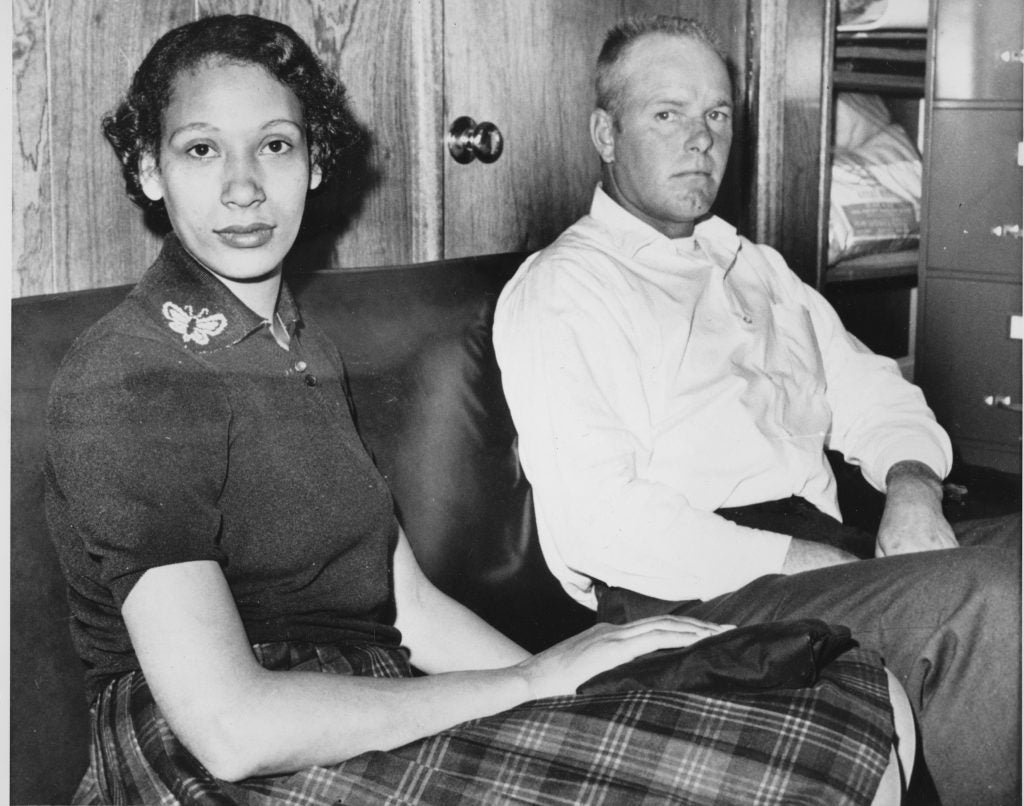 A black and white image of a dark-skinned woman and a light skinned man sitting side by side.