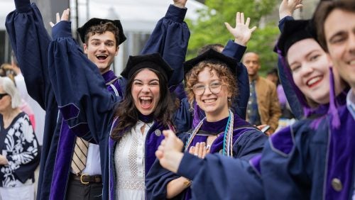 A group of graduates cheers and celebrates.