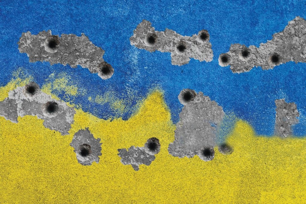 Photo of a wall painted in the Ukrainian national colors of blue and yellow, and pockmarked with bullet holes