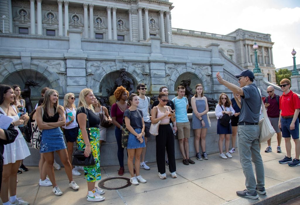 A group of students standing outside the Library of Congress, listening to a man leading a tour