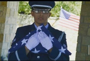 A young man in Air Force uniform, holding a folded U.S. flag.