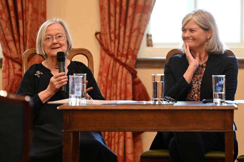 Two older women seated at a table, participating in a panel discussion
