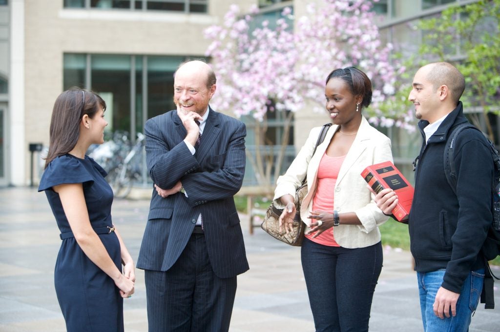 A man in a suit speaking with two young women and a young man