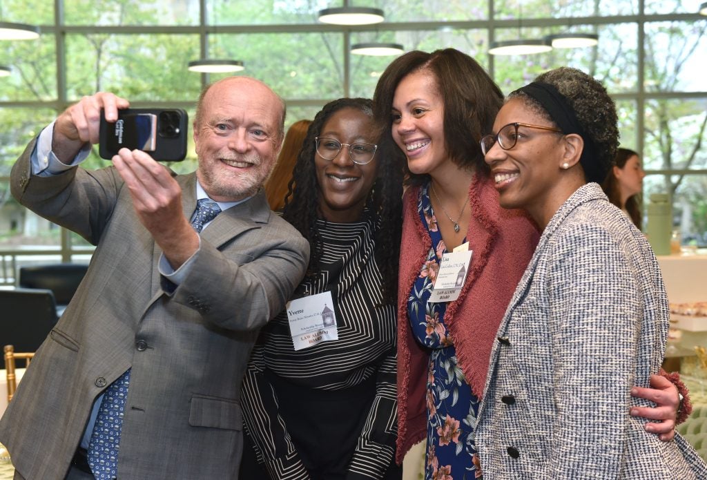 A man and three women posing as the man takes a selfie photo of the group