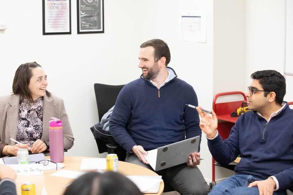 Instructor Adam Smith sits with students during the course simulation exercise. 
