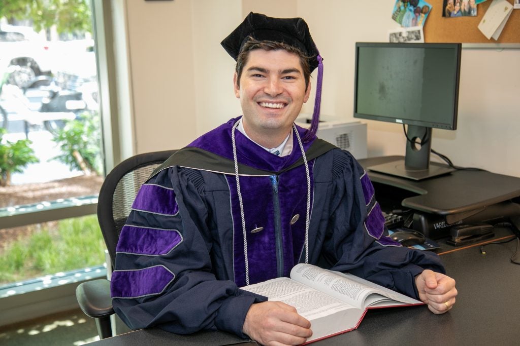 Trey Wolf sits at his desk wearing regalia.