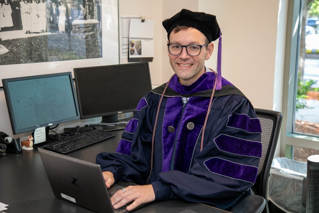 Nick Opinsky sits at his desk wearing regalia.