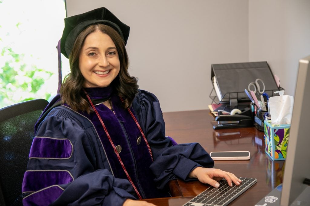 Kelsey Levin-Epstein sits at her desk wearing regalia.