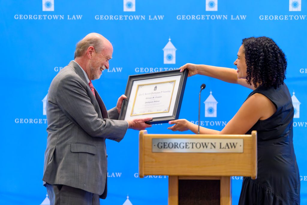A man smiles as a woman hands him a framed certificate