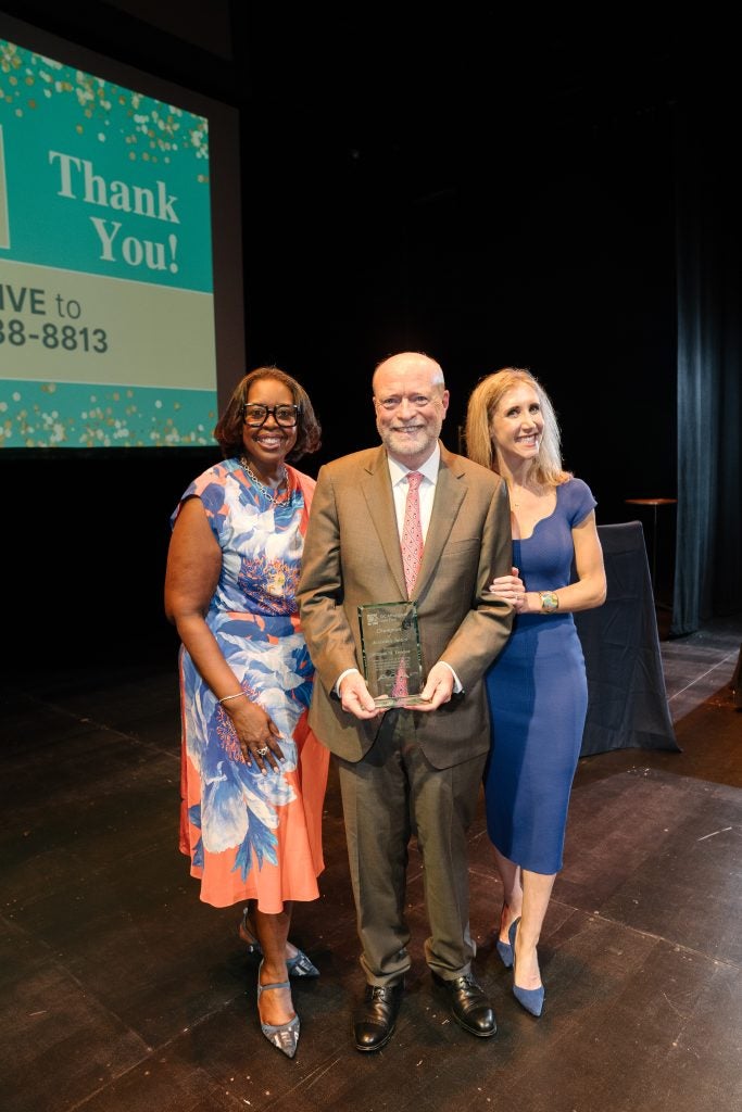 Three people standing together, one holding an award
