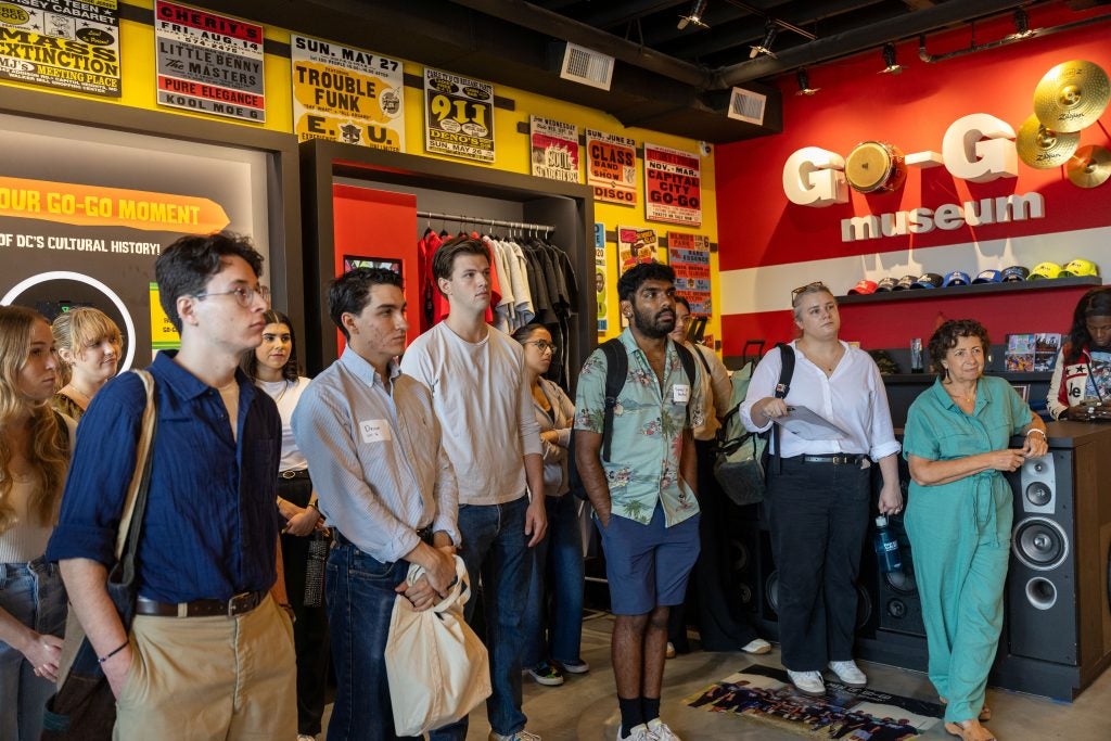 A tour group in a colorful room displaying artifacts and information about go-go music