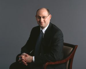 A man in a dark suit sitting in a wooden chair