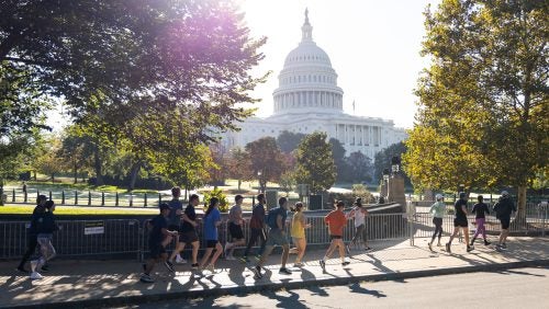 Runners on the sidewalk pass the U.S. Capitol building.