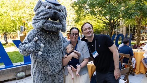 Two adults and a baby pose with the Jack the Bulldog mascot.