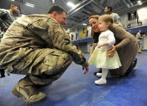 Casey Doss wears his U.S. Army combat uniform and crouches down to speak to a young girl.