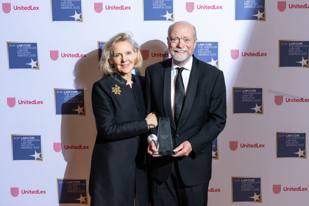 A woman and man standing together. He is holding an award.