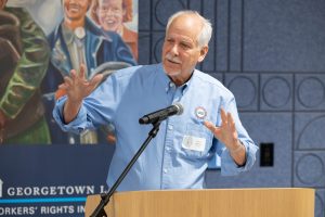 A man in a blue shirt speaking at a microphone