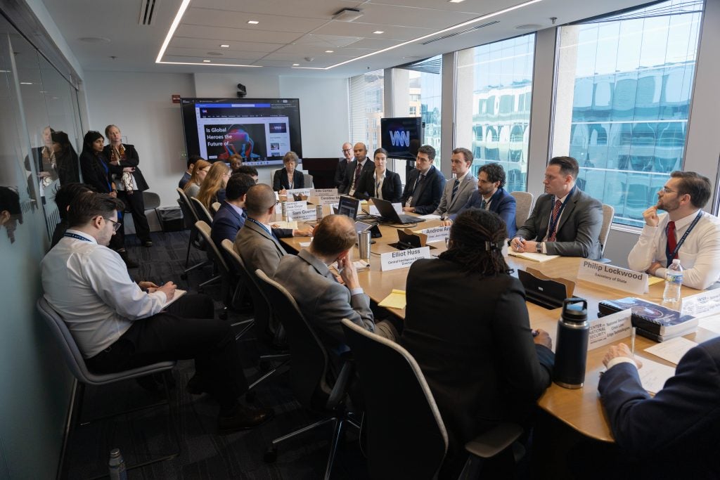 More than 20 people, including students, control team members and CNS staff sit or stand in a conference room during a presidential briefing meeting. 