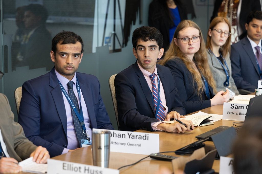 A row of students sit next to each other at a conference table in the briefing room and listen attentively.