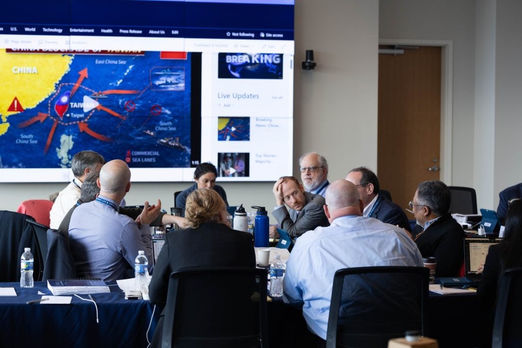 Approximately 10 "control team" members sit around a conference room table, engaged in deliberation.