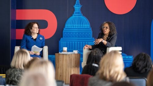 Two women speakers sit in front of an audience on the dais.